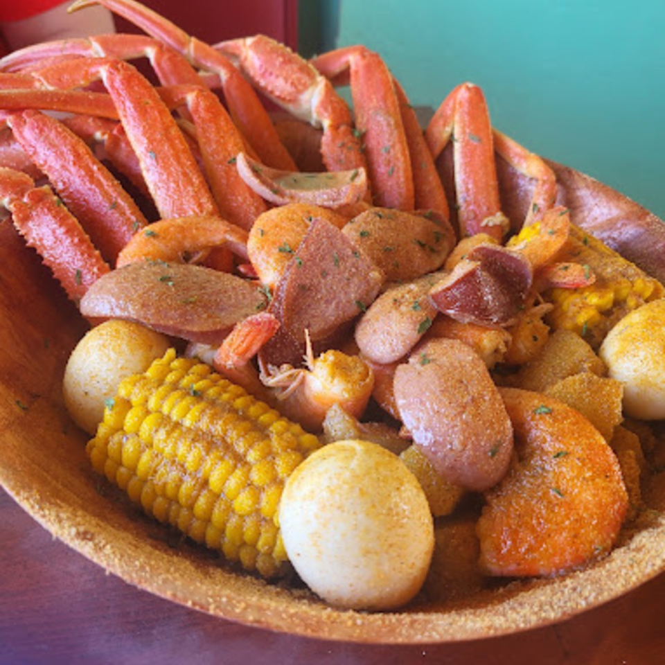 A seafood boil with crab legs, shrimp, corn on the cob, and potatoes in a wooden bowl.
