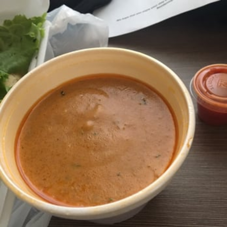 A bowl of Crab Stop II's creamy seafood bisque with a side of lettuce and sauce.