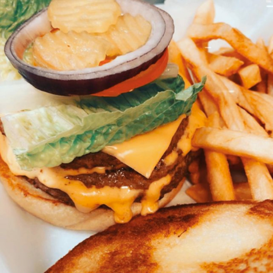 A double cheeseburger with lettuce, tomato, onion, pickles, and a side of french fries.