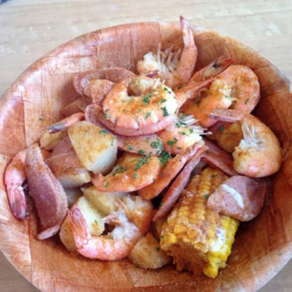 A wooden bowl filled with seasoned shrimp, corn on the cob, and red potatoes from Crab Stop II.