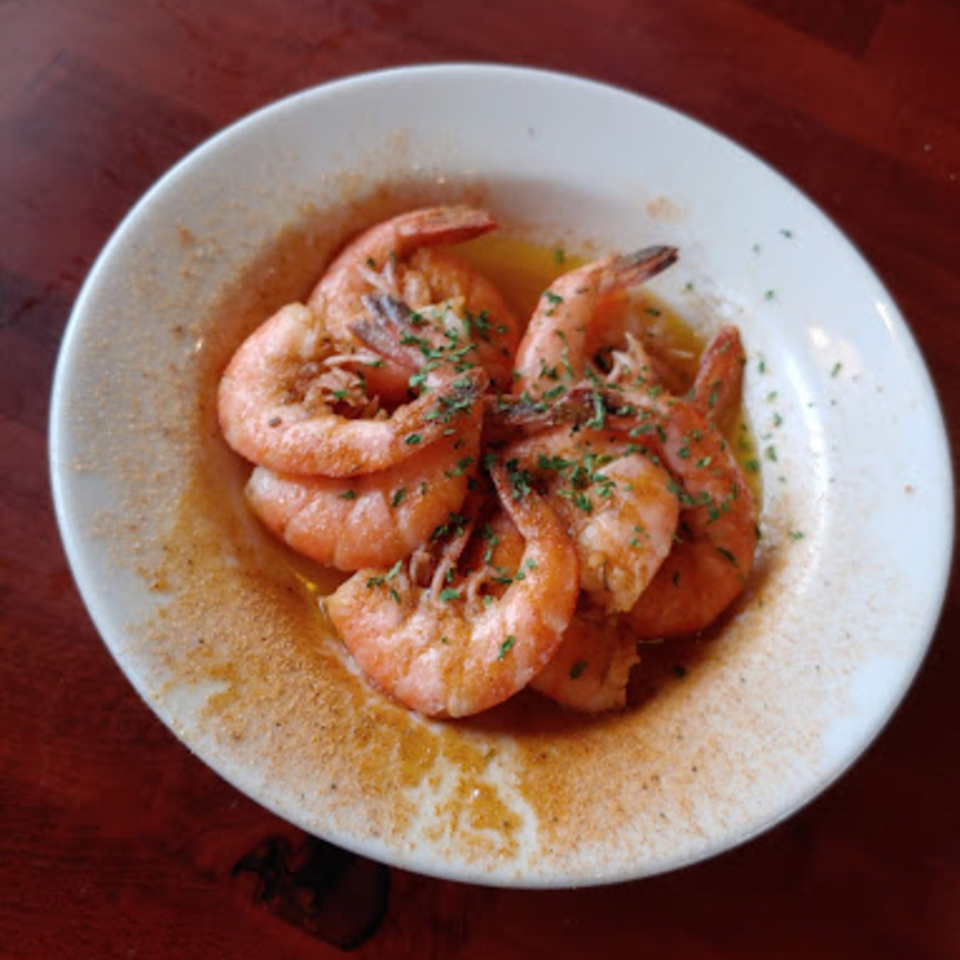 A white bowl filled with seasoned shrimp in a buttery sauce, garnished with parsley.