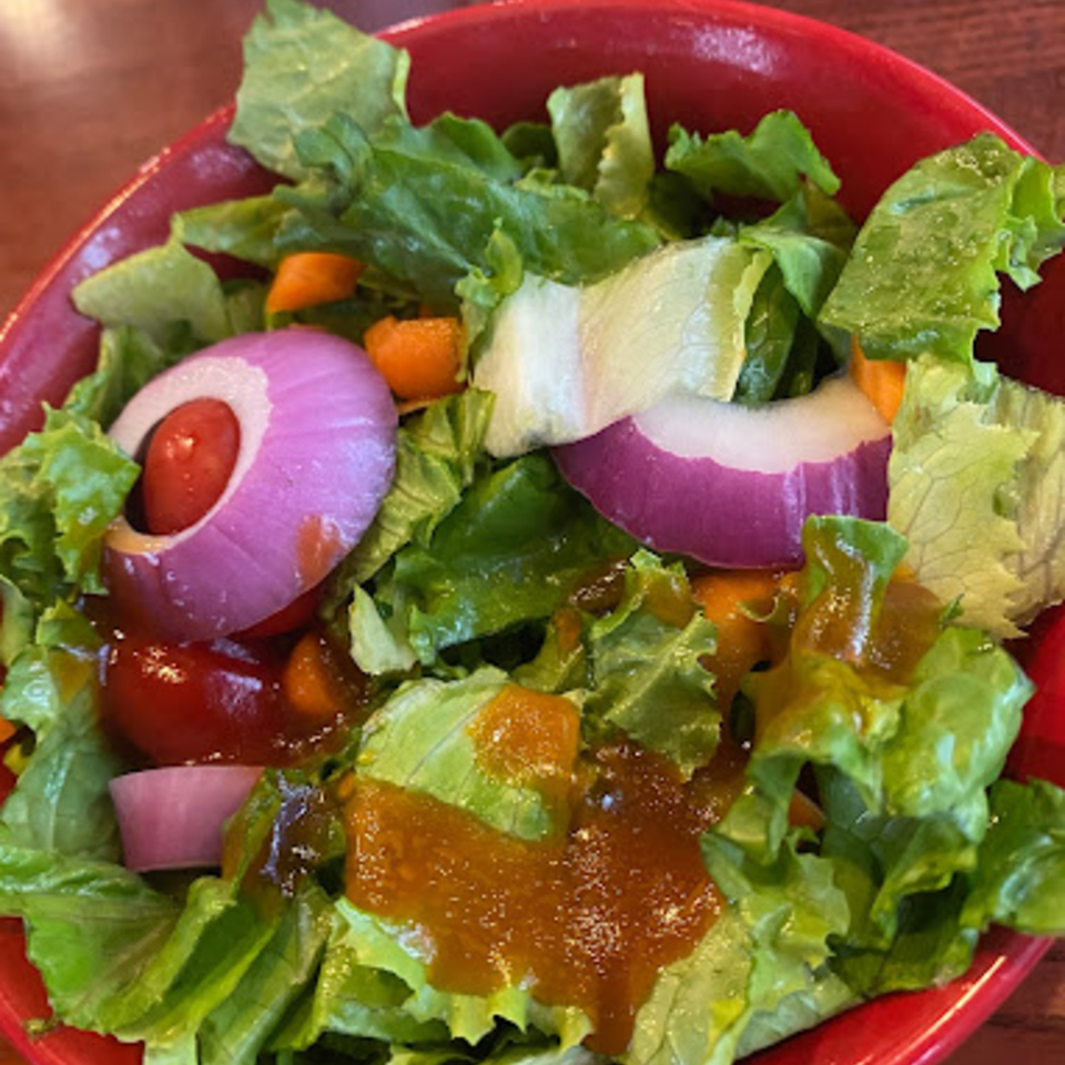 Fresh green salad with red onion, cherry tomatoes, and orange dressing in a red bowl.
