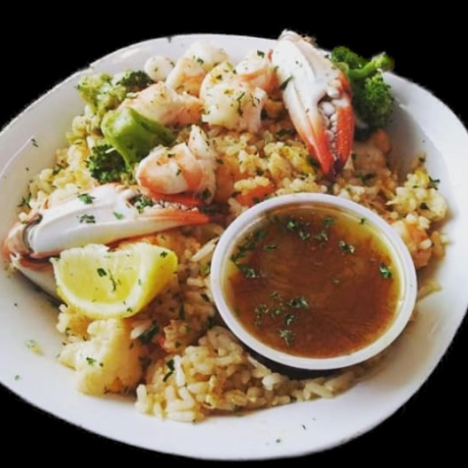 Seafood rice with shrimp, crab claws, broccoli, lemon, and a side of sauce.